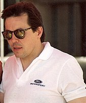 Alan Kulwick wearing black sunglasses over his eyes and a white T-shirt with a car company's logo on its left