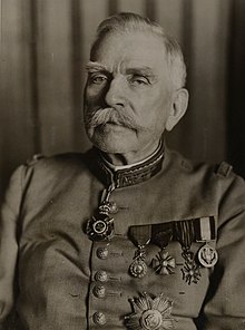 Photographie noir et blanc d'un homme moustachu, âgé, en uniforme militaire. De nombreuses décorations sont visibles sur son torse.