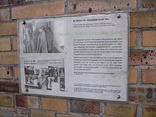 Farbfotografie von einer Gedenktafel mit dem Titel „Depot für Aktion Entartete Kunst“. Rechts steht ein Text und links sind zwei Schwarzweißfotografien. Auf einem betrachtet Hitler die aufgereihten Gemälde im Lager und auf dem zweiten Foto sind die Gemälde ausgestellt.