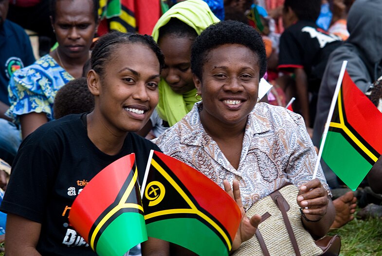 Photograph of two women smiling and holding small plastic Vanuatu flags