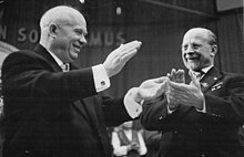 Two smiling men raise bouquets of flowers over their heads.