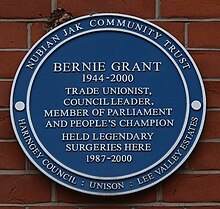 Blue plaque reading: "Bernie Grant 1944–2000 Trade Unionist, Council Leader, Member of Parliament and People's Champion held legendary surgeries here 1987–2000". Inscribed around the border is: "Nubian Jak Community Trust / Haringey Council / Unison / Lee Valley Estates"