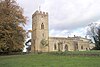 A stone church seen from the south, with a tower surmounted by a battlemented parapet on the left, and the nave with a porch and the chancel to the right