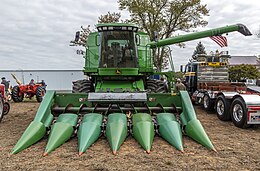 Vooraanzicht van een groene maaidorser met plukvoorzetstuk. De losvijzel, waar een Amerikaanse vlag aan wappert, is uitgeklapt.