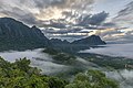 Montagnes karstiques, nuages colorés et brume au lever du jour, vue sud depuis le sommet du mont Nam Xay, durant la mousson, à Vang Vieng.