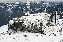 Petit bâtiment au design moderne sous la neige avec un paysage alpin en arrière-plan.