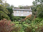 a garden with hedges and shrubs overlooked by a house