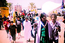 Photograph of a crowd, with some banners and stands in the background and some people in comstumes.