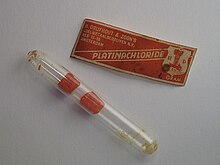 Two rough red crystals in a glass tube, next to a worn leathery red and white label saying "platina chloride"