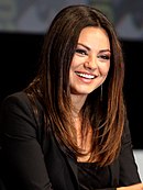 A woman with black hair, smiling while wearing a black dress.