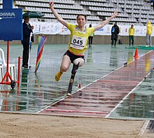 Athlète handisport atterrissant au saut en longueur, de face, les bras en l'air.