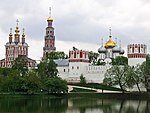 A walled monastery with red and white towers with golden domes