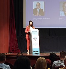 Sofia Zacharaki speaking at the podium of the EuroPride 2024 Human Rights Conference in Thessaloniki 2024 with other speakers and audience in the photo