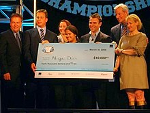 A high school student stands behind a large blue check. Behind her stand six adults in suits. The check has a National Vocabulary Championship logo in the top left and is written out to Aliya Deri for the amount of $40,000. The check is dated March 10, 2008.