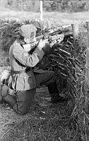 A soldier in a shallow trench, aiming a gun