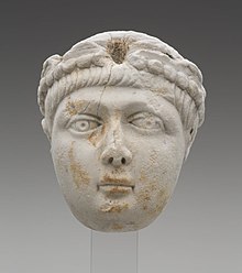 A Miniature portrait head of a young boy with a full face and short, straight hair. He wears a pearl-edged diadem, which identifies this head as portrait of an Emperor. The head greatly resembles depictions of the Theodosian princes. This marks the identification of the head to be either Honorius, Arcadius, or Valentinian II.