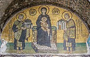 A mosaic painted golden yellow. One crowned man each is standing on the right and left, both are offering models of large buildings to a woman seated on a throne holding her baby. All four people have halos, Greek letters can be seen, possibly labels describing the people