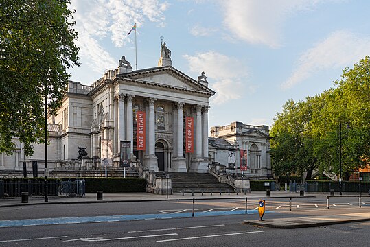 Tate Britain building seen from the footpath along the Thames, in evening light.