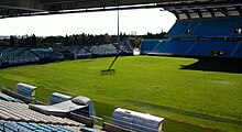 Stade de football sans aucun joueur, ni aucun spectateur. Une partie du stade est dans la pénombre.