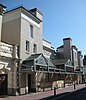 A white stuccoed building with three-storey towers flanking a central recessed entrance bay with "HIPPODROME" on a panel beneath a parapet. A low glazed roof spans the façade.