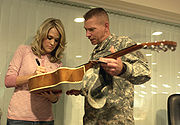 Army Master Sgt. Ricky Bakke holds his 10-year-old daughter’s guitar for country music star Carrie Underwood to sign at Camp Arifjan, Kuwait (13 December 2006)