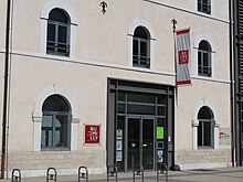 Photographie en couleurs et de légèrement en biais de la façade d'un bâtiment gris et beige