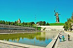 Monument depicting a woman with a sword in the background, a pond with a Cyrillic inscription at the side in front