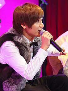 Leeteuk speaking into a michrophone and facing right