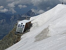 Deux refuges à la limite d'une arête neigeuse et de la paroi rocheuse.