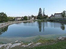 Une pièce d'eau entourée de plusieurs mini murets de pierre recouverts chacun de deux pierres plates posées en V très ouvert