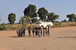 Kinderen in een vluchtelingenkamp in El Geneina in West-Darfur, met achter hen een pantserinfanterievoertuig van UNAMID, in november 2009.