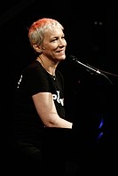 Annie Lennox tampil dengan sebuah piano, tersenyum.