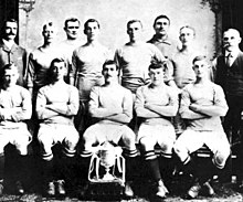 A group of thirteen men, eleven in association football attire typical of the early twentieth century, and two in suits. A trophy sits in front of them