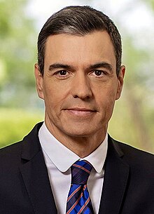 (Top image): Pedro Sánchez staring at the camera with a neutral expression, in a suit and a neck tie with the colors blue, black, & yellow arranged in a tartan like pattern. (Bottom image): Pedro Sánchez' signature