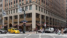 Base of the facade as seen from the southwest corner of Fifth Avenue and 45th Street. The first three stories are clad in stone with metal storefronts, while the upper stories are clad in brick.