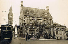 Three-storey Victorian building festooned with garlands with the words "God Save the King" mounted on the pitched roof