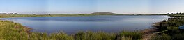 A lake with reeds and a hill beyond