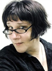 A middle-aged Caucasian woman with medium-to-short black hair and glasses peers at the camera.