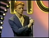 A red-haired man in a suit standing next to a microphone