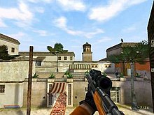 Screenshot from a first-person perspective, showing the player's character on a mission, looking out from a window, at a hotel across the street in Morocco. An assassin can be seen on a rooftop, getting ready to assassinate a person.