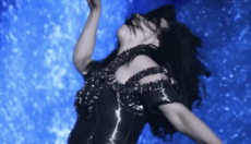 Whilst wearing a shimmering black outfit, Björk is shown twirling her arms while blue lava erupts behind her