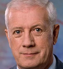 Late middle-aged man with grey hair wearing a white dress shirt and a grey suit jacket