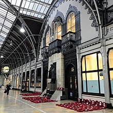 Wide view of a railway platform with a statue set against a wooden background