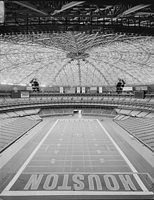 The interior of a football stadium. The stadium is empty and covered by a large, dome-like roof; the ends of the playing field have large letters spelling "Houston".