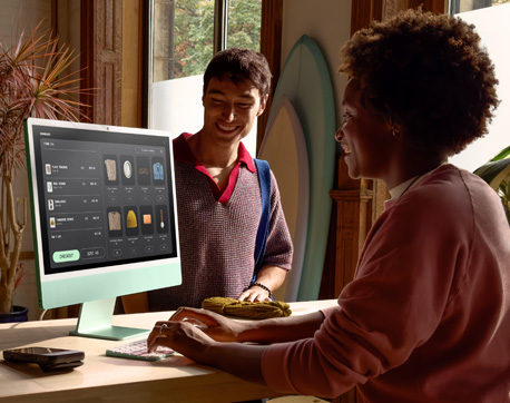 Bright room with two people. A woman uses an iMac featuring nano-texture glass display, while a man sits nearby