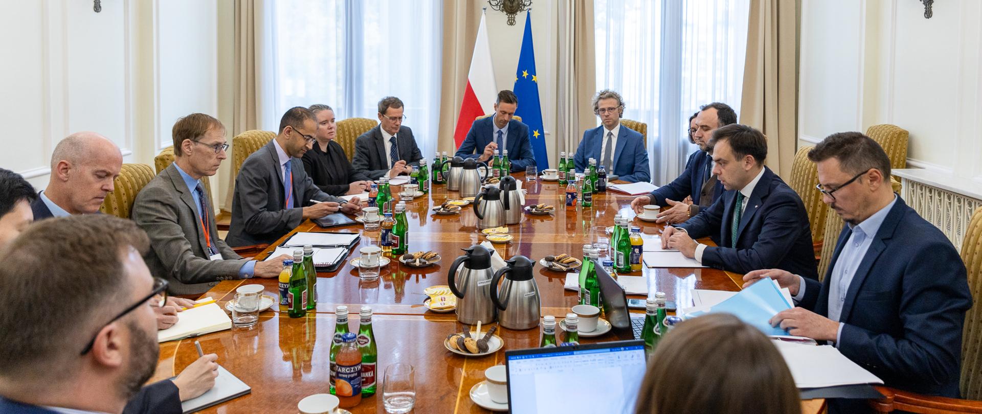 Minister finansów Andrzej Domański, wiceminister Paweł Karbownik na spotkaniu z przedstawicielami Międzynarodowego Funduszu Walutowego, siedzą przy stole, w tle flagi Polski i UE