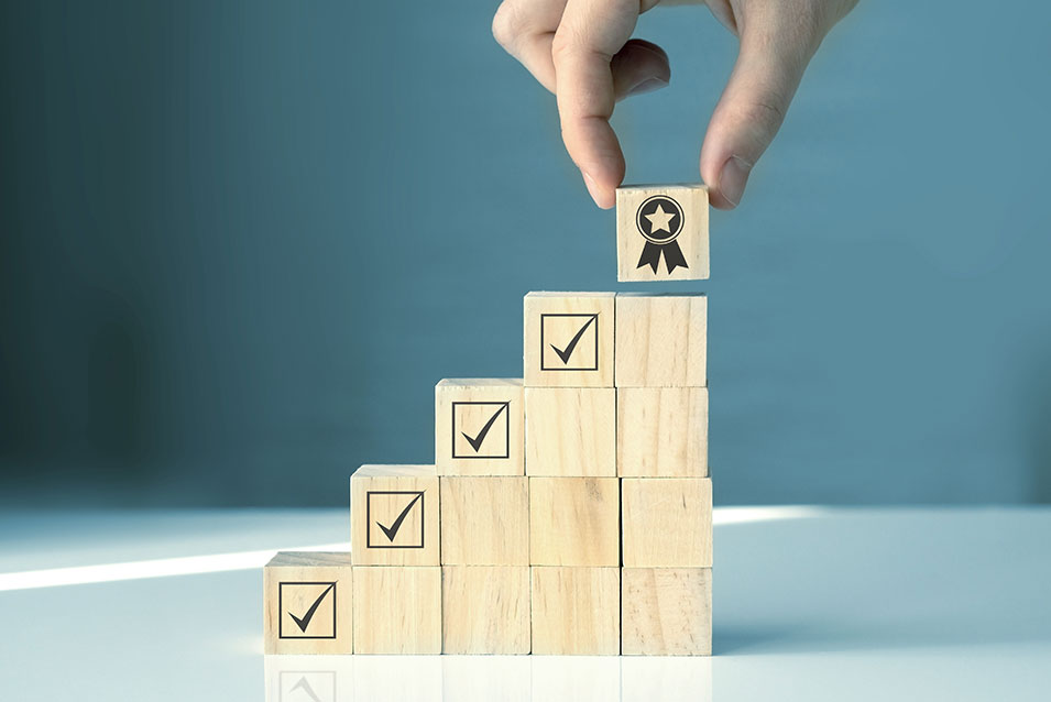 A stack of blocks marked with check marks creates stairs to the top block, which has a certification ribbon on it.