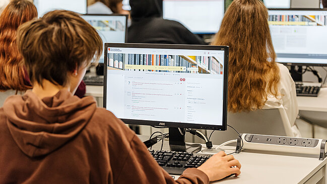 Foto von Person, die an einem Computer arbeitet, von hinten.