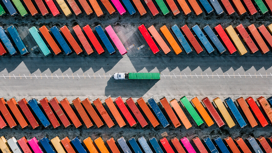 Overhead view of a truck hauling a shipping container driving between rows of shipping containers