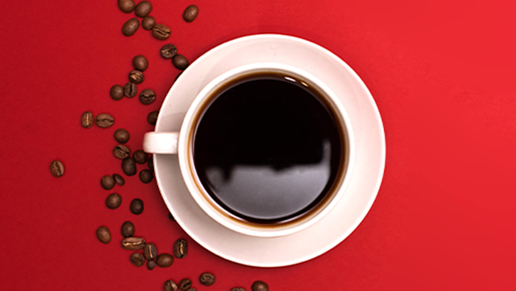 Overhead view of coffee in a white cup on a saucer with coffee beans scattered around